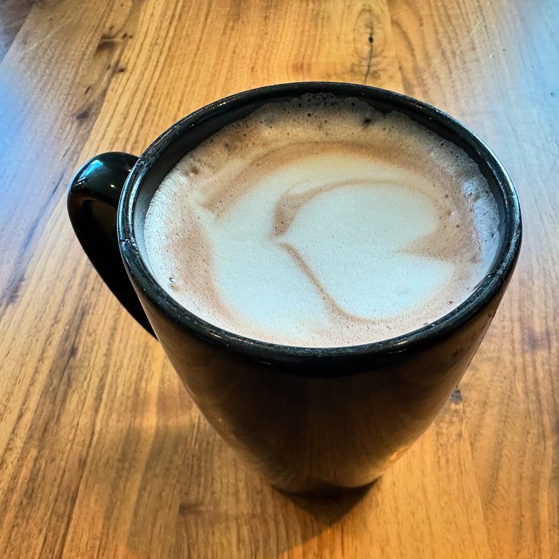 Black mug with a soft milk swirl on warm plank wood