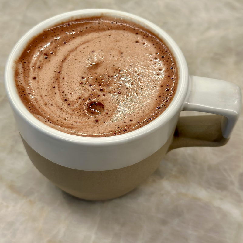 Hot chocolate with a swirl in a two-tone mug on pale marble