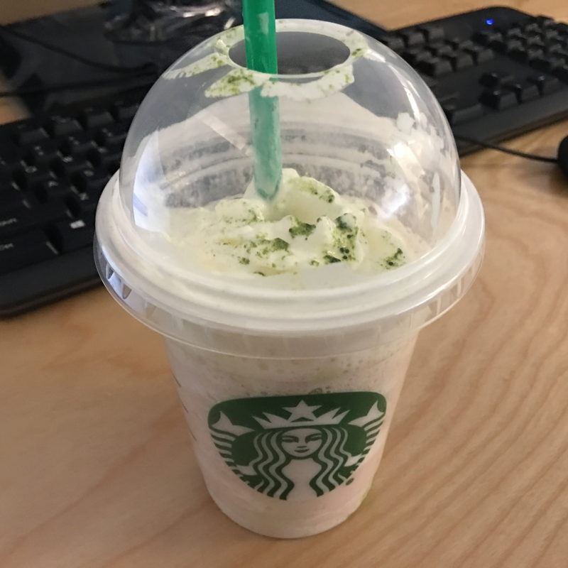 Green-tea-topped Frappuccino under a dome lid on a pale wood desk beside a keyboard