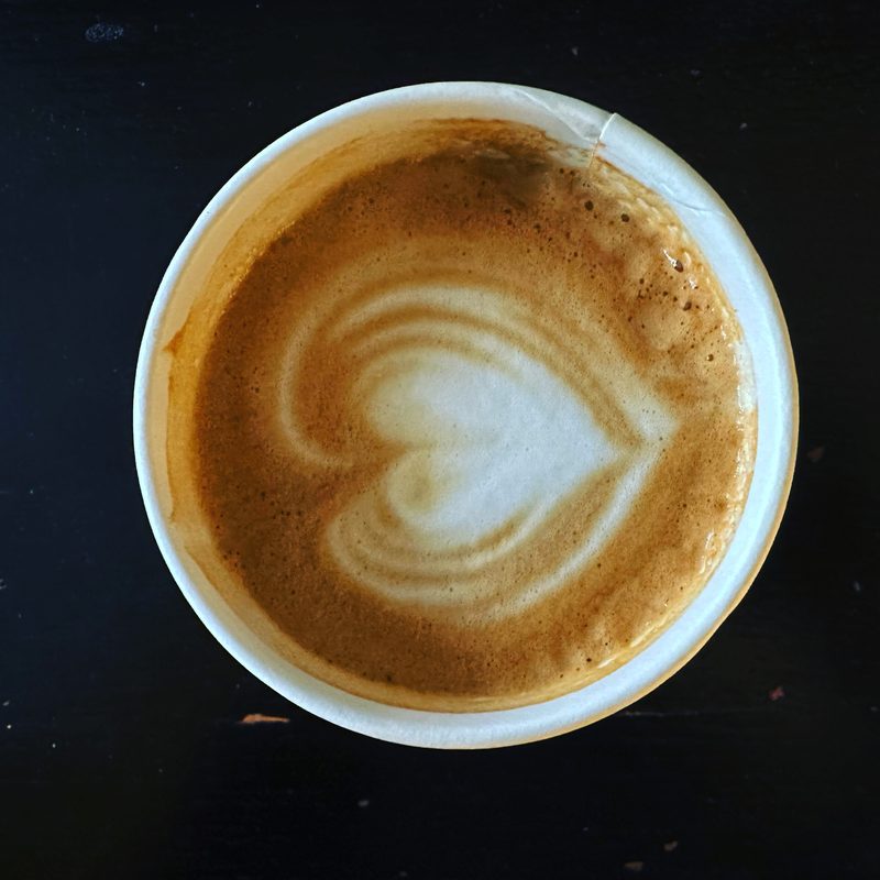 Heart latte art in a white paper cup on a matte black table