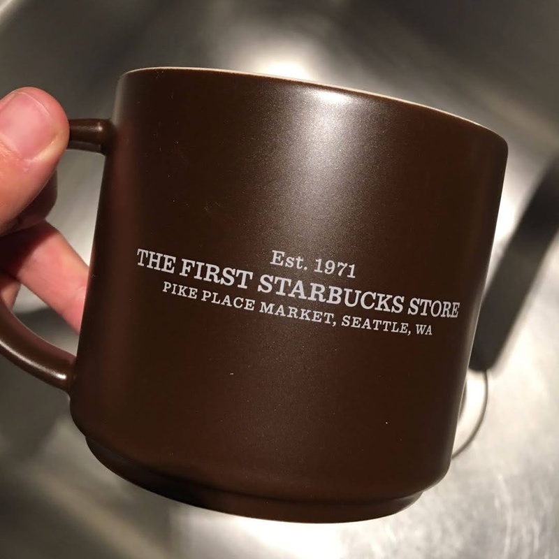 Brown mug engraved The First Starbucks Store, Pike Place Market, Seattle, held in hand