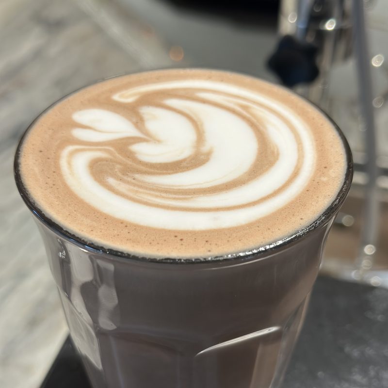 Tall glass mocha with a swirl on a black tray at a marble counter