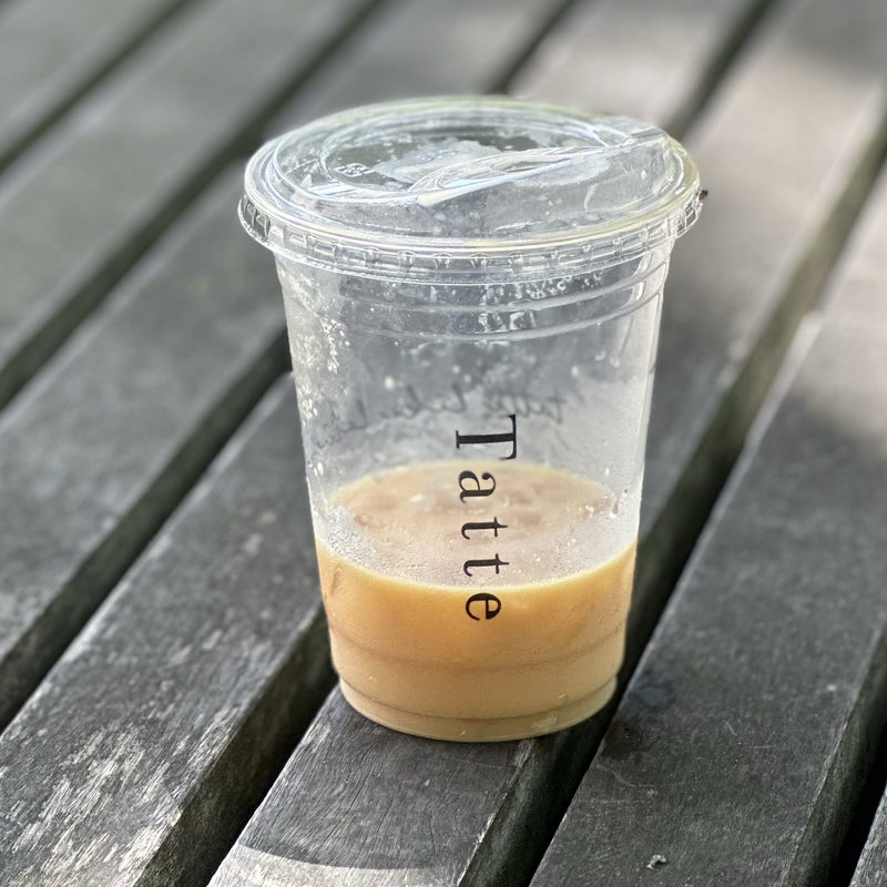The last of an iced latte in a Tatte cup on a weathered picnic table